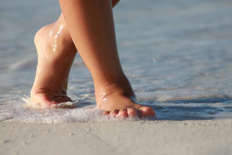 a person walking in the ocean with her feet close to the water