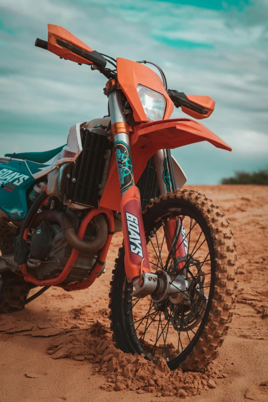 a orange dirt bike sitting on top of a sandy road