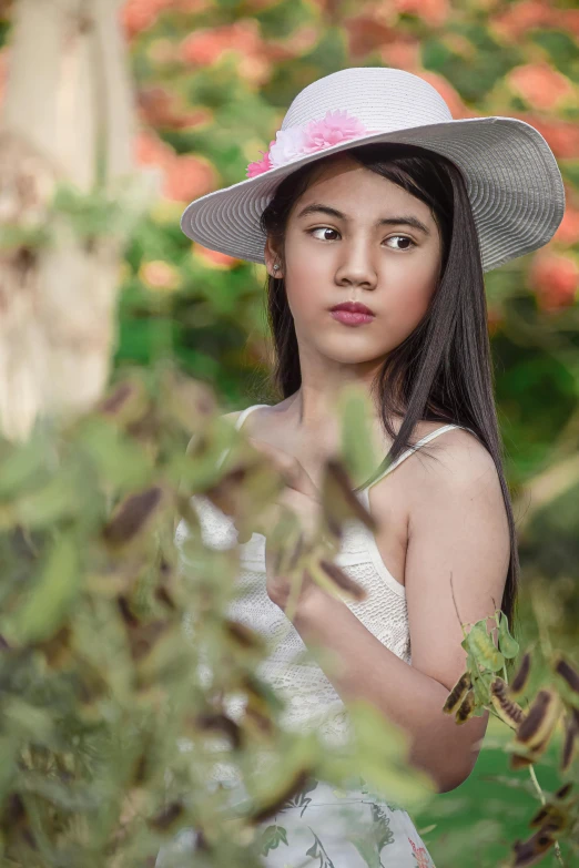 girl wearing a white dress and big hat standing by flowers