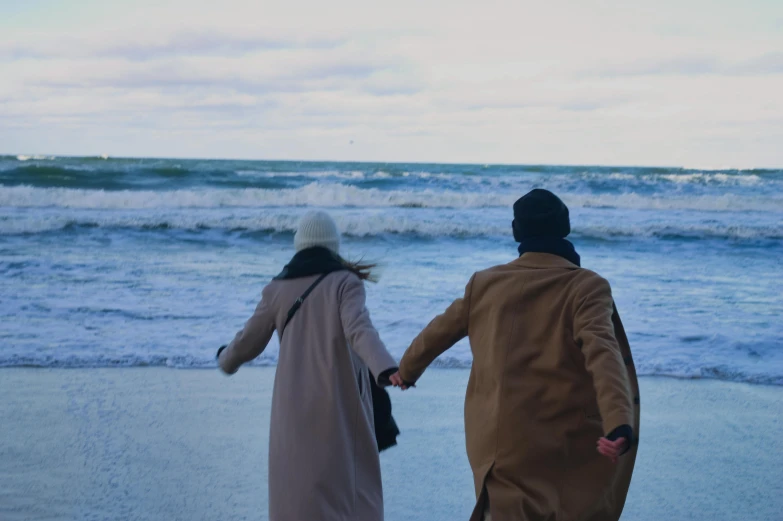 two people hold hands and walk down the beach