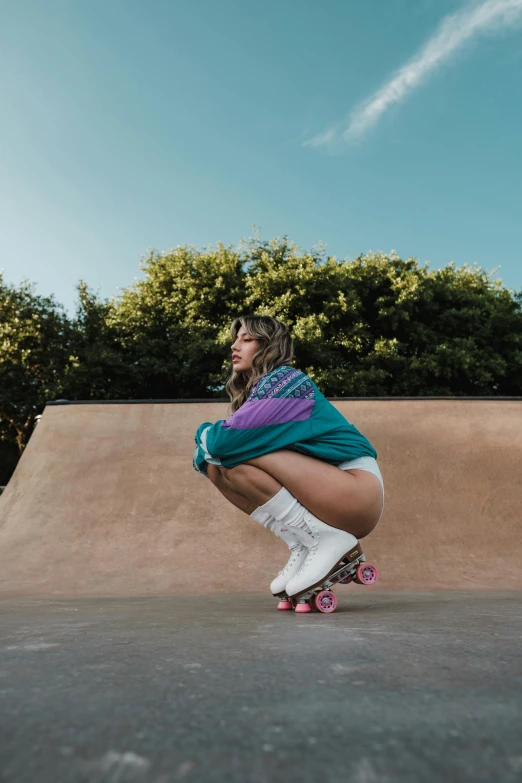 young woman crouched down, wearing kneepads and knee socks with white skateboard on flat ground with trees in background