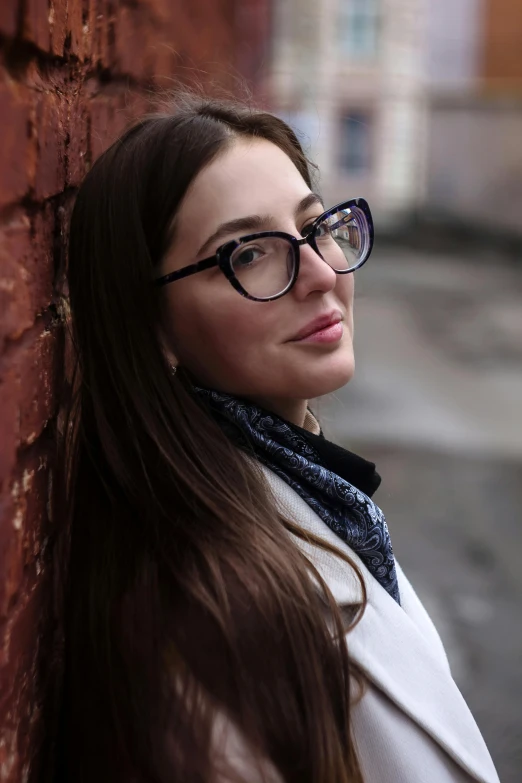 a woman in glasses leaning against a brick wall