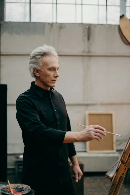 an older man holding a stick standing next to a easel