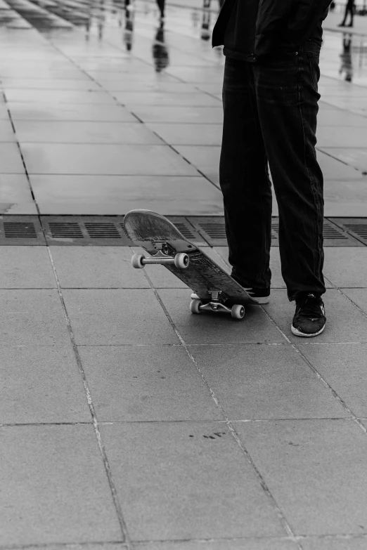 person's legs with black shoes stand in front of their skateboard