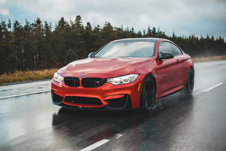 red bmw sports car driving on wet road near woods