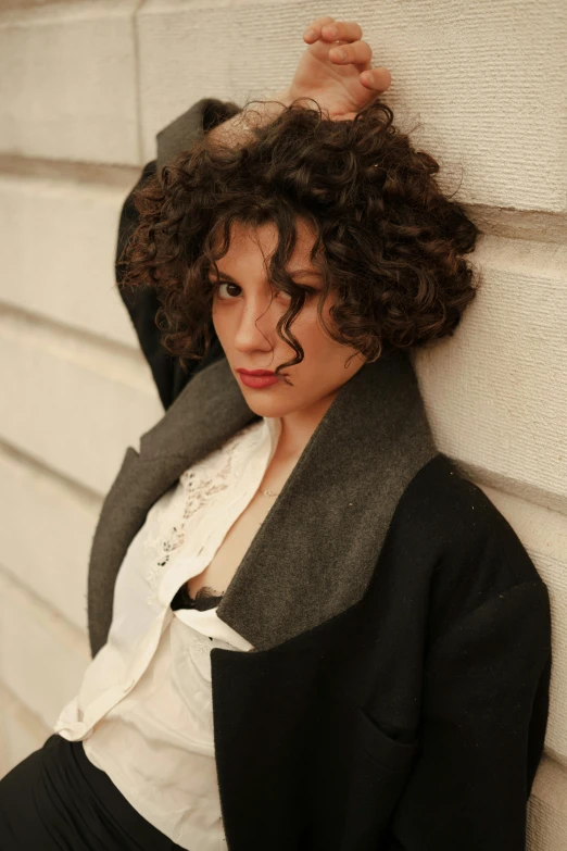 an attractive young woman leaning on a white wall