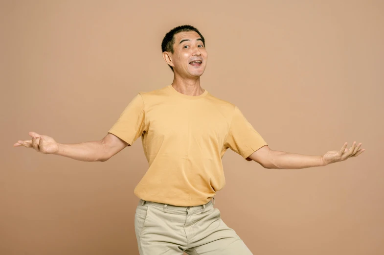 a man in an orange shirt and khaki pants is posing with his arms outstretched