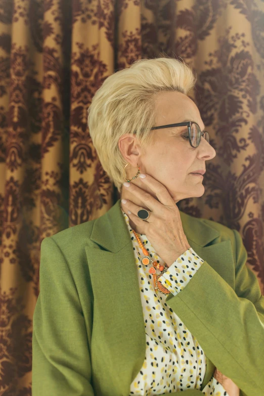 a woman with glasses sitting against a curtain