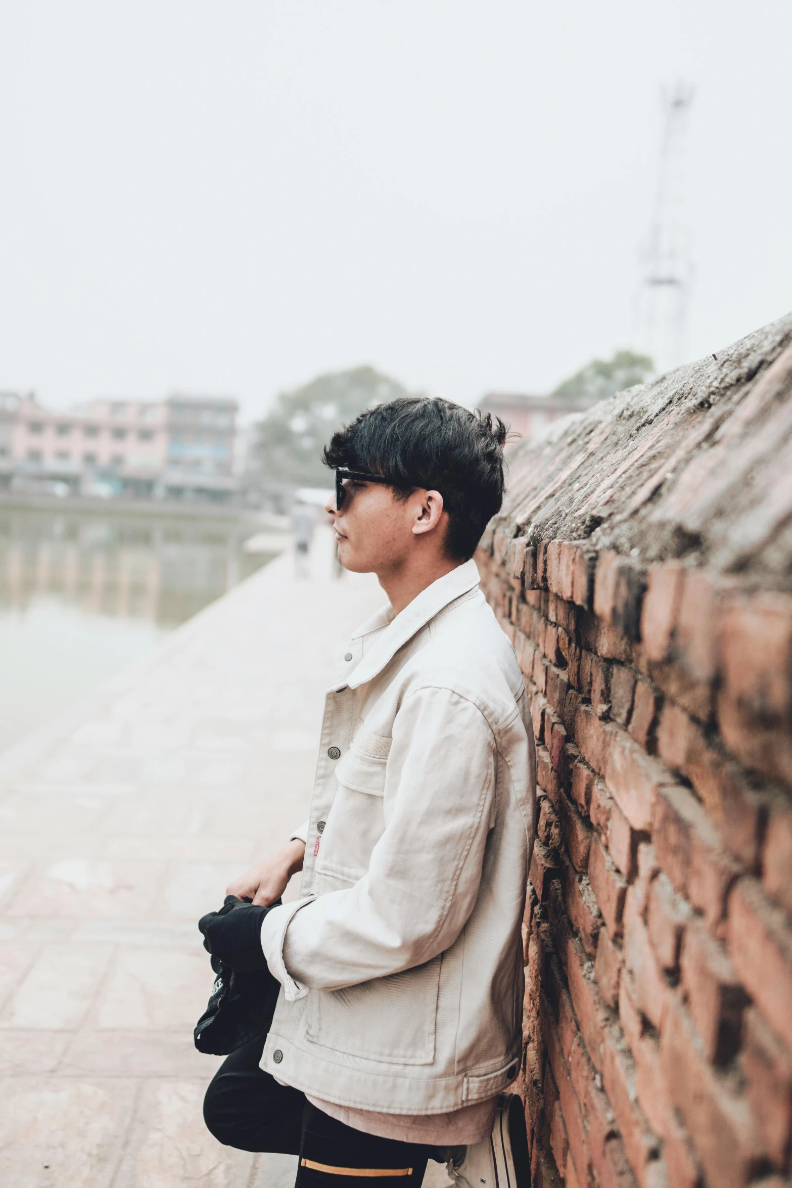 a young man in glasses leaning on a brick wall