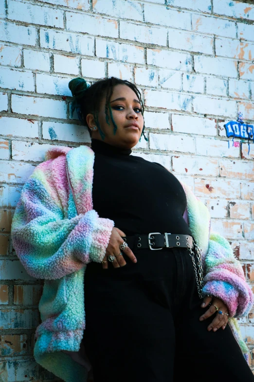 a black woman wearing a pastel jacket, standing against a brick wall