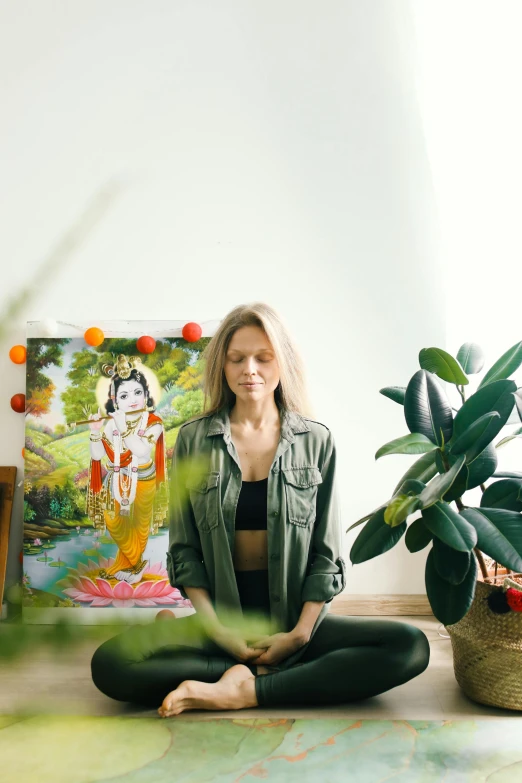 a woman sitting in a yoga position with a painting behind her