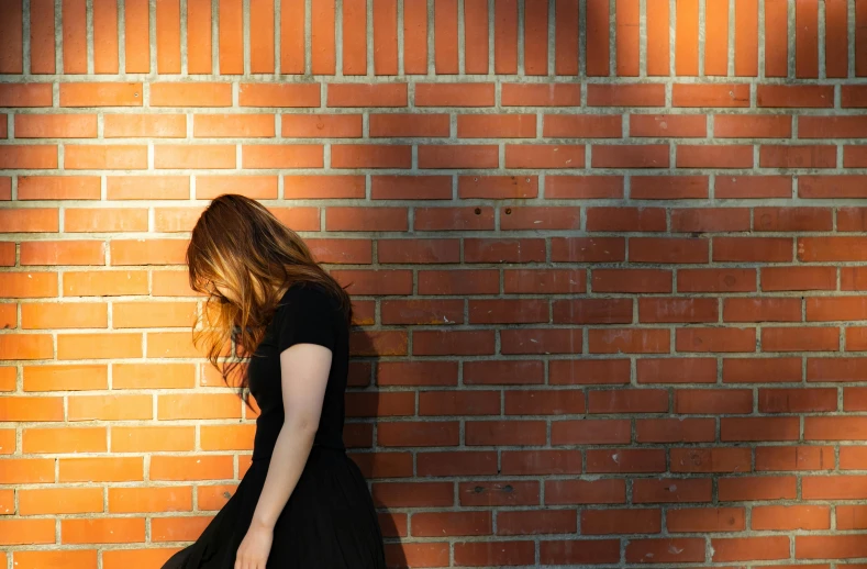 the woman is standing near a brick wall with her hand on a bag