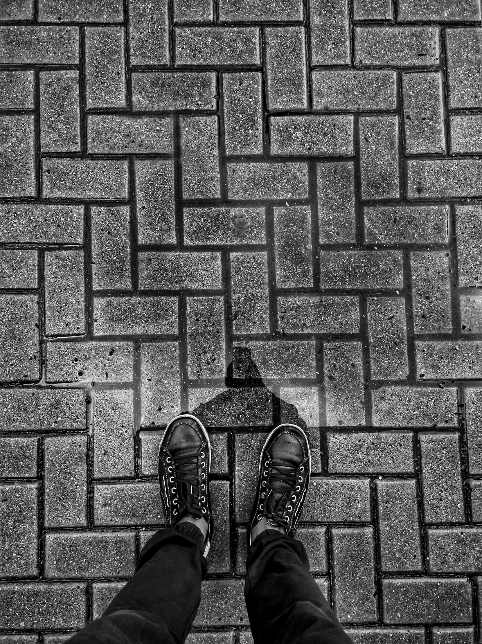 a pair of feet standing on top of a sidewalk next to a brick wall