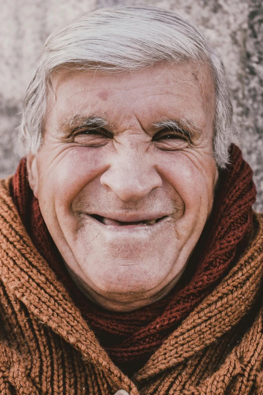an old man wearing a brown and orange sweater smiles at the camera
