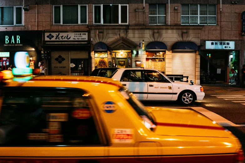 taxi cabs sit in traffic near shops and businesses