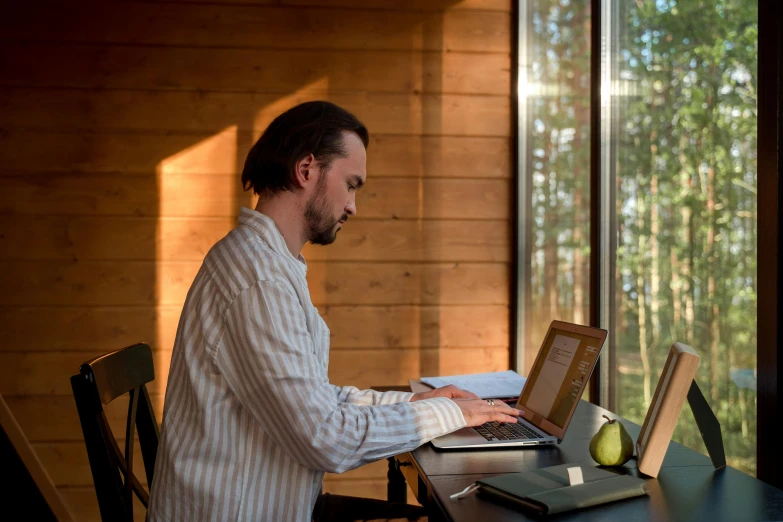 a man with long hair in white shirt sitting at table using laptop