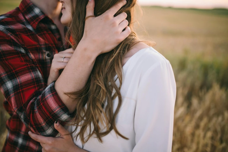 the man is kissing his lady while she stands in a field