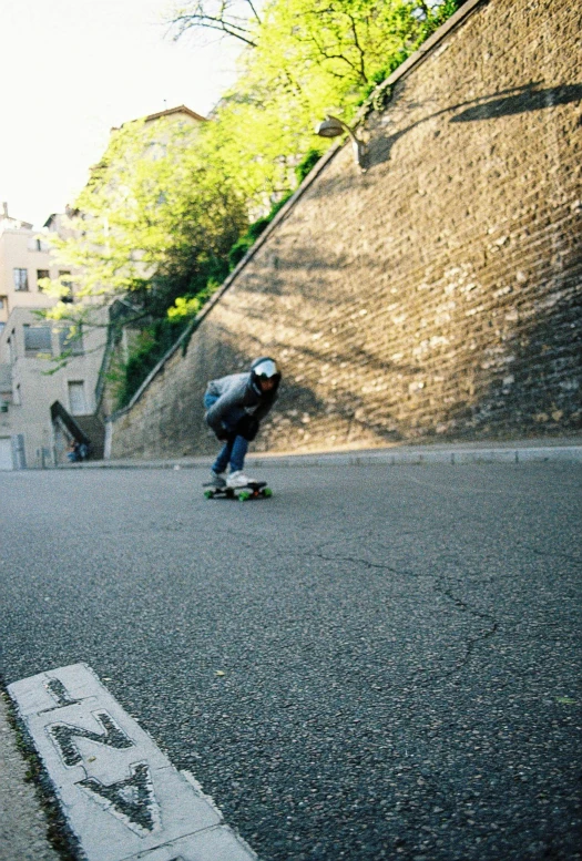 the skateboarder is going down the street wearing blue jeans and a helmet