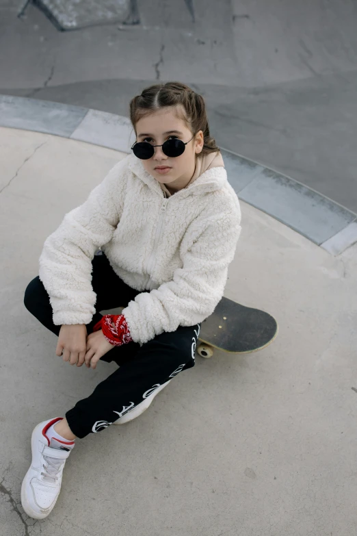  sitting on concrete with skateboard near her feet