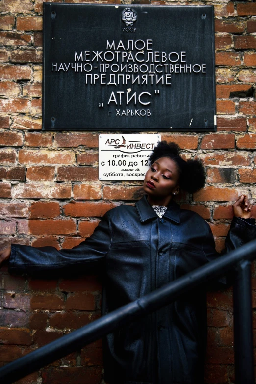 a young black woman posing for the camera by a brick wall with sign saying memorial of david g thomas and memorial of eva marie