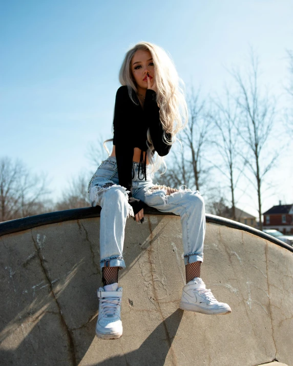 a woman wearing ripped jeans and high top shoes sitting on a skateboard ramp