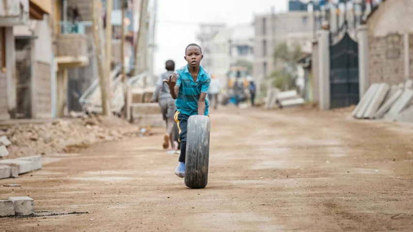 a boy running with a large tire down a dirt road