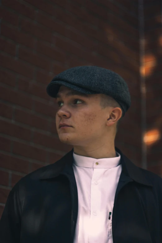 a young man standing near a brick wall