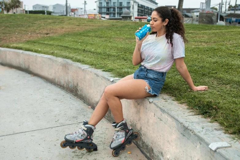 girl in skates leaning against cement wall, drinking water