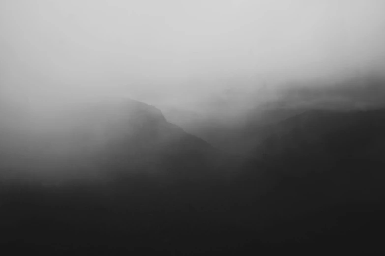 a black and white picture with hills covered in fog