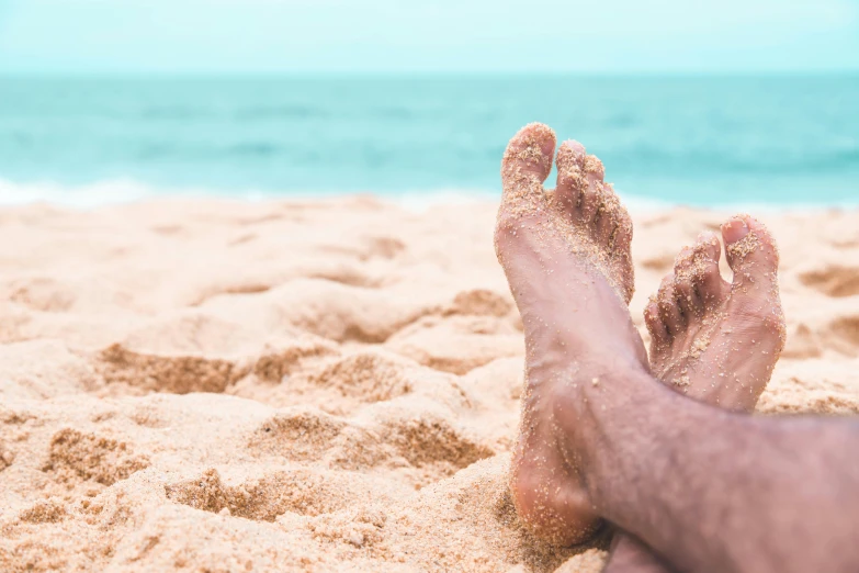 a persons feet sticking out in the sand at the beach