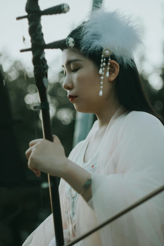 woman in asian dress holding a large stick with white feathers on it