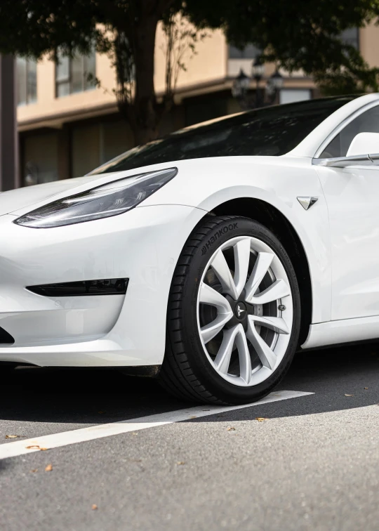 a white electric car on the street with it's lights on