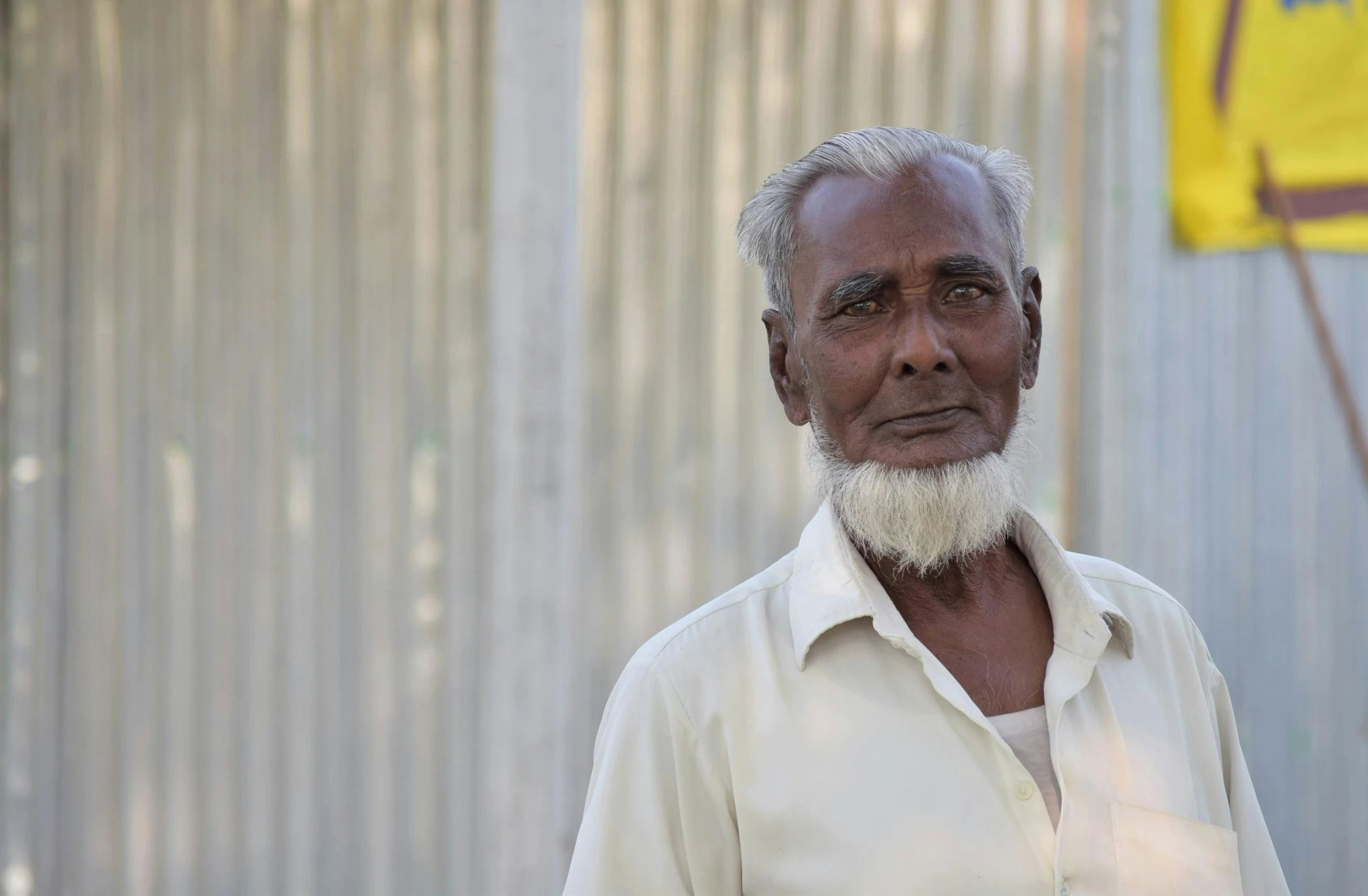 a man wearing a white shirt and a white beard stands in front of a yellow flag