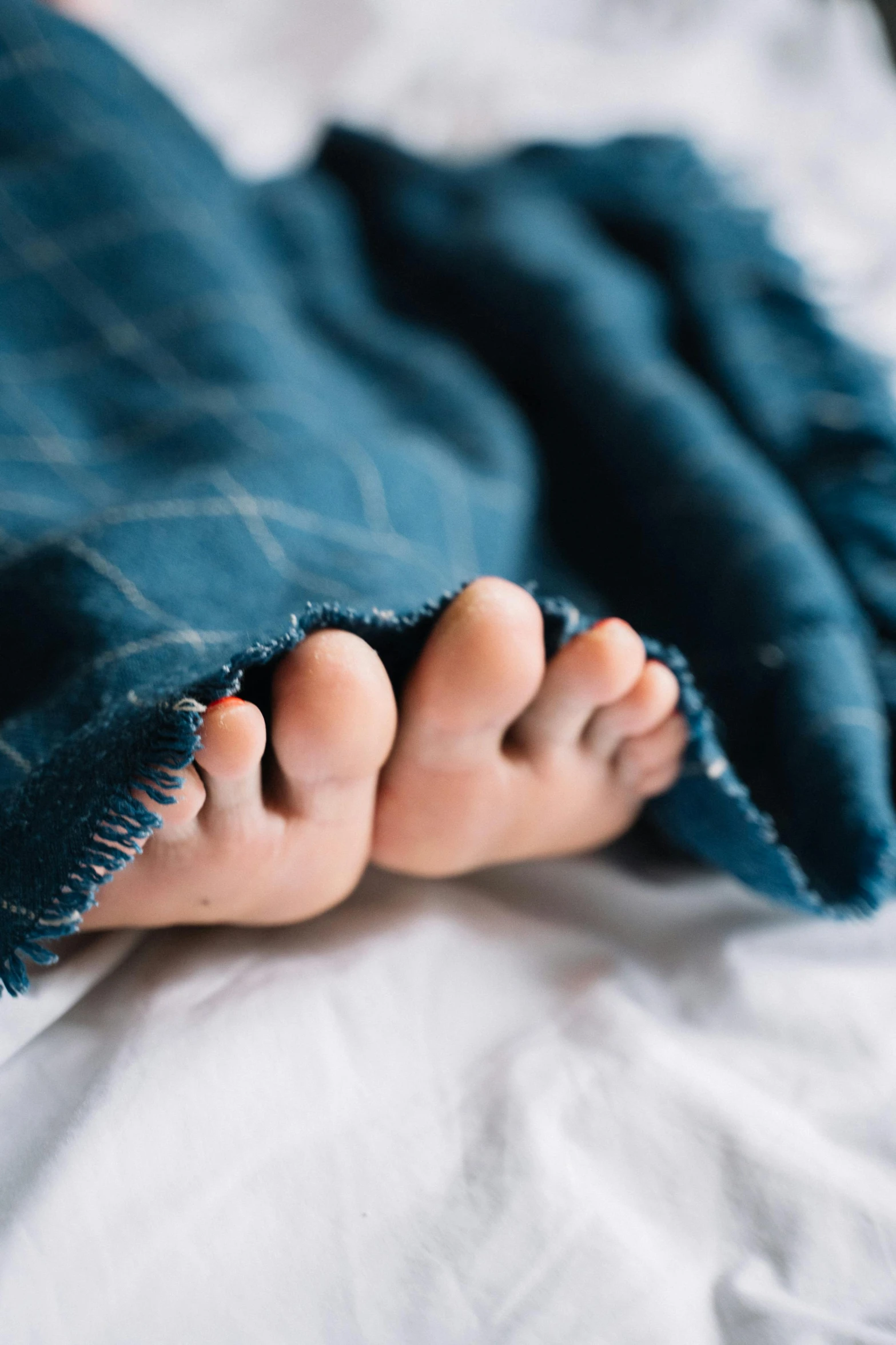 bare feet under blue plaid blanket laying on bed