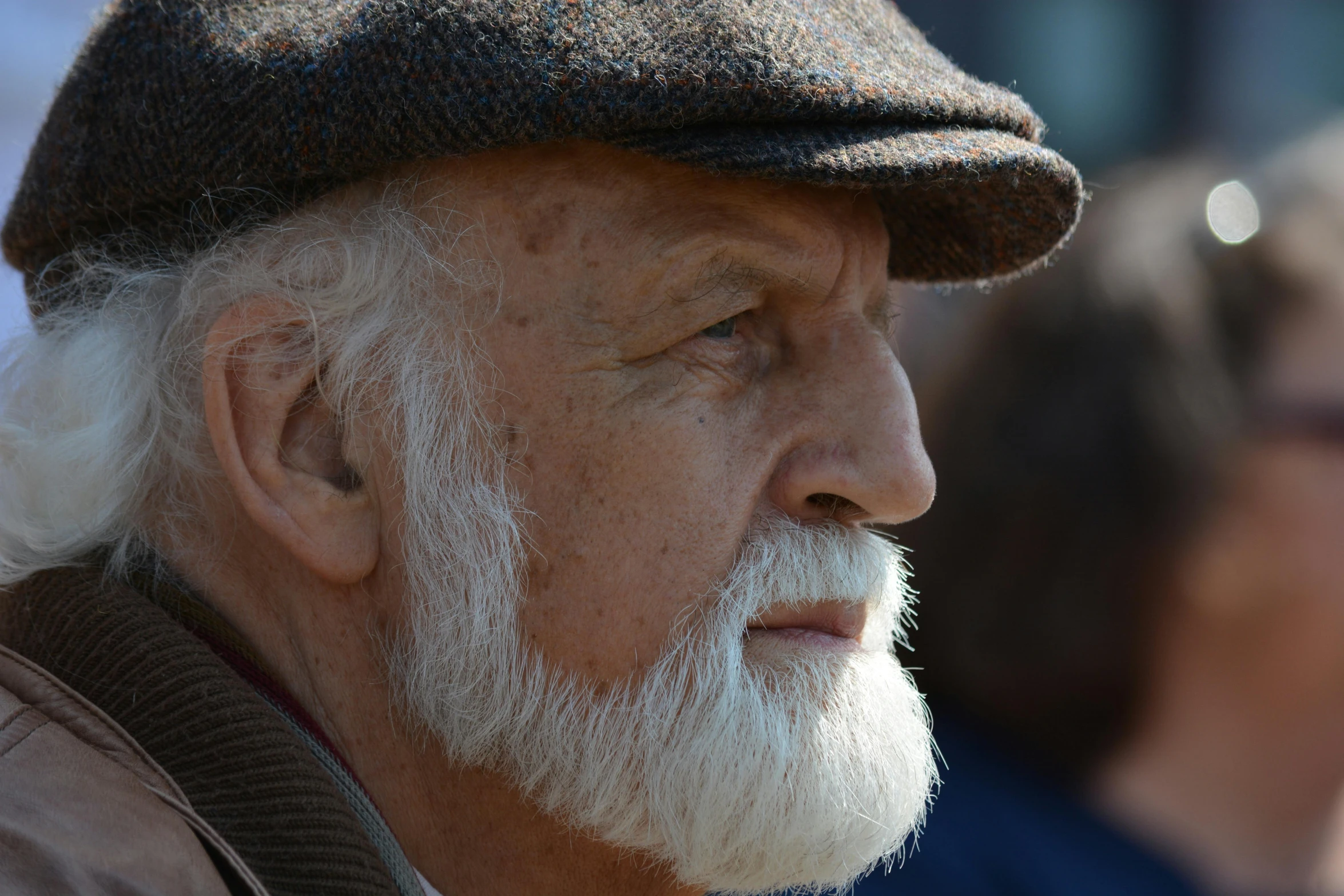 an old man wearing a hat looks away from the camera