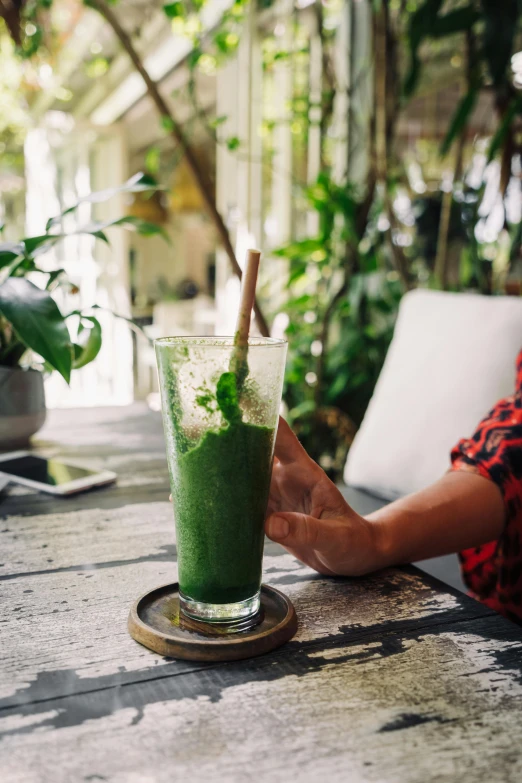 a man is sitting outside at a table drinking a green drink