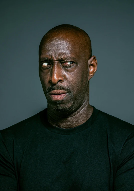 a black man wearing a black t shirt and looking at the camera