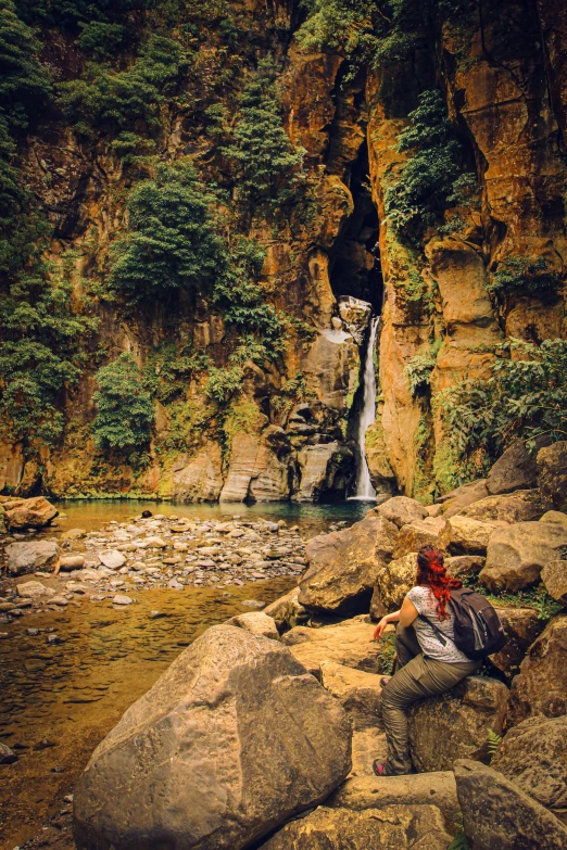 a person sitting on rocks in front of a waterfall