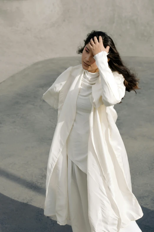 woman in white standing against cement wall, covering her eyes