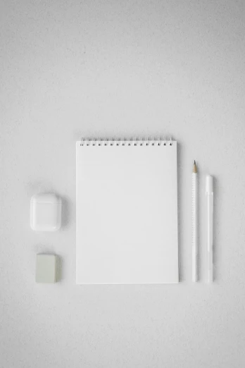 a white notebook, pen and eraser on a gray surface