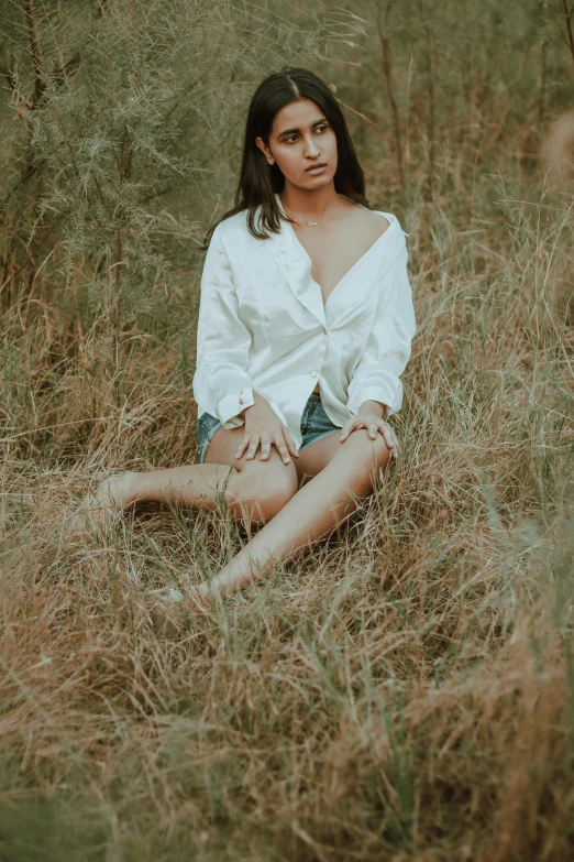 a girl sitting in tall grass wearing a white shirt