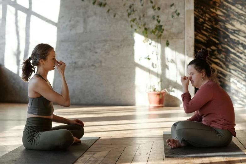 two girls sit side by side on the floor, one has her face pressed to her lip while the other holds her chin up