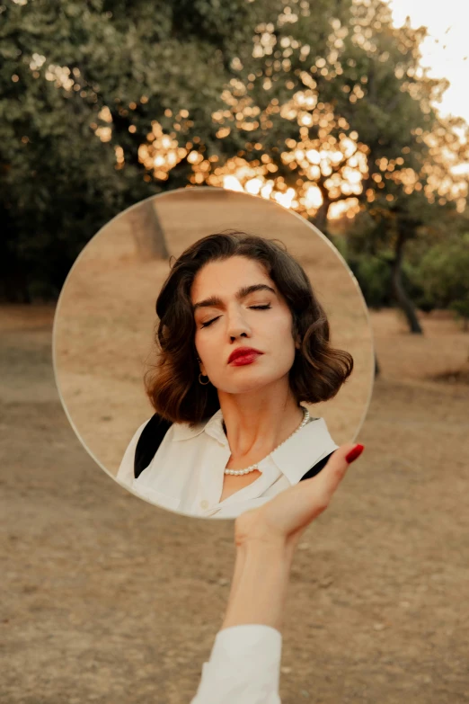 a girl holds a circle mirror showing her face with both hands