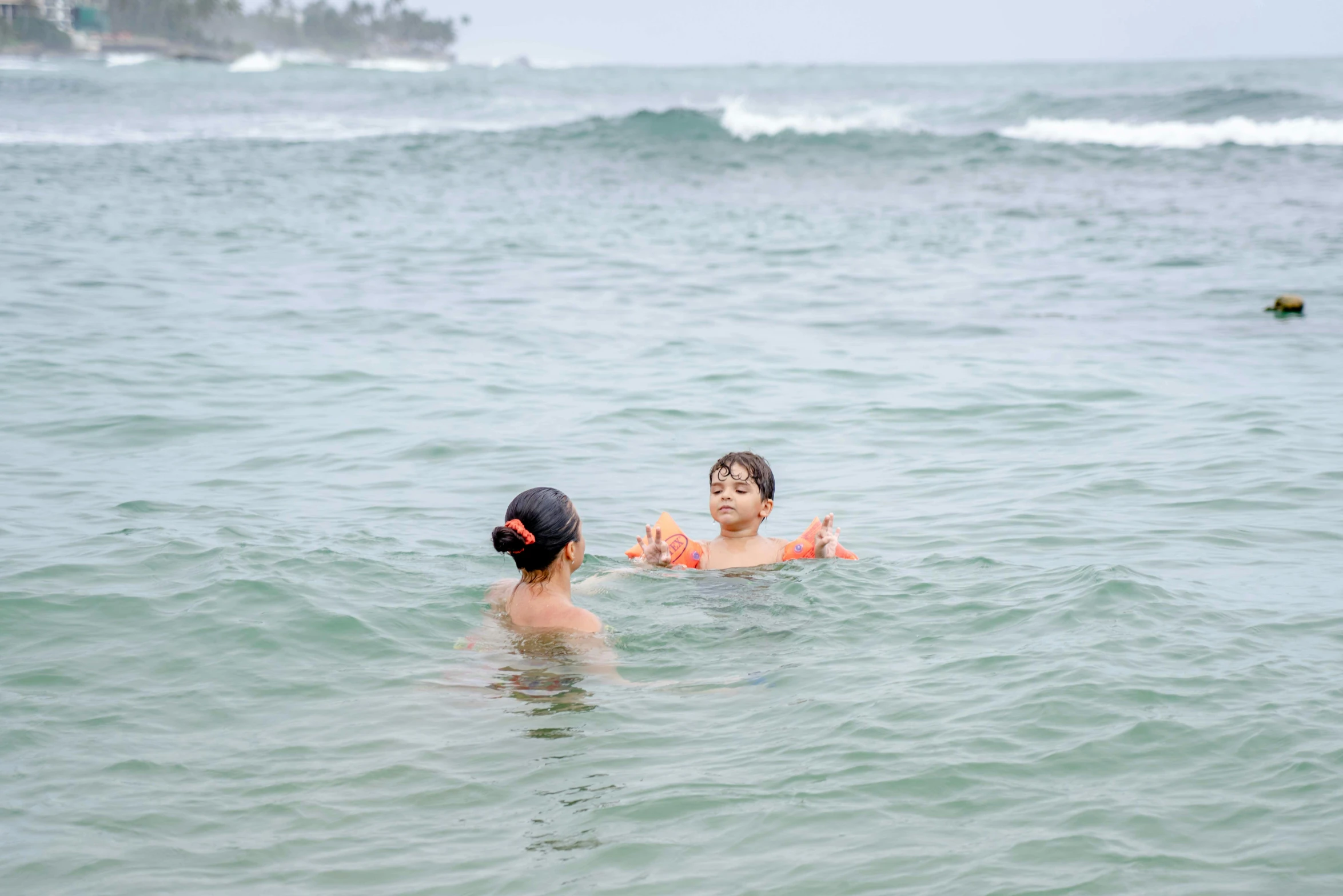 two people in the ocean with a small boat in the distance