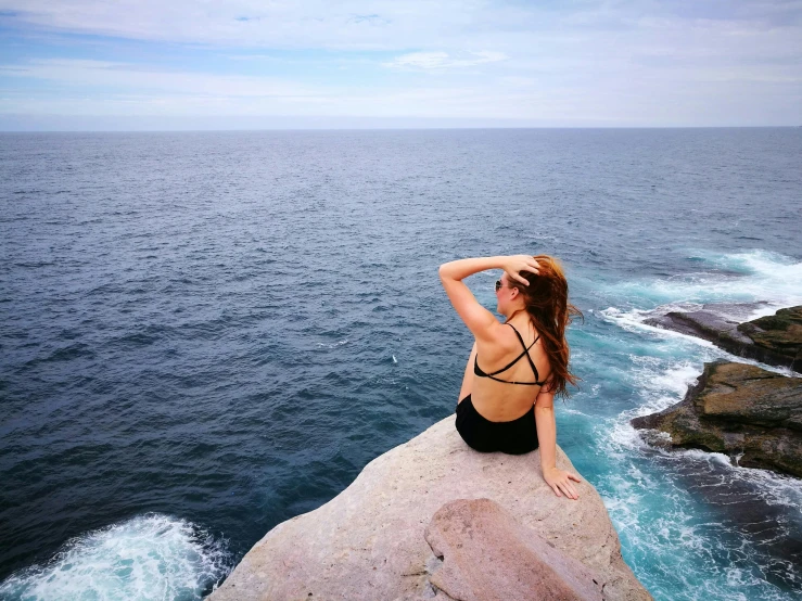 a beautiful red haired woman sitting on top of a rock