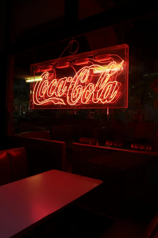 a large neon coca cola sign hangs on the wall of a restaurant