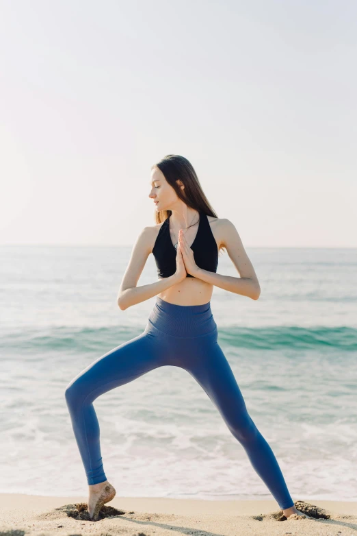 woman in blue sports outfit doing yoga on the beach