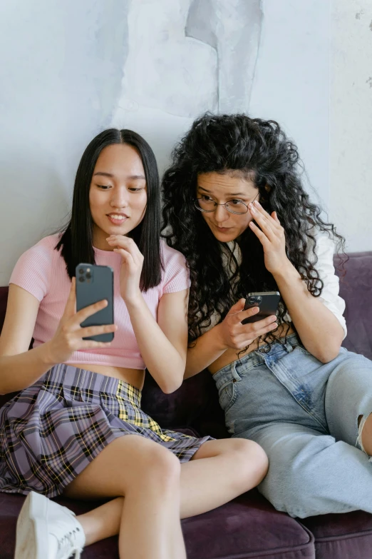 two young women sitting next to each other, one using a cell phone