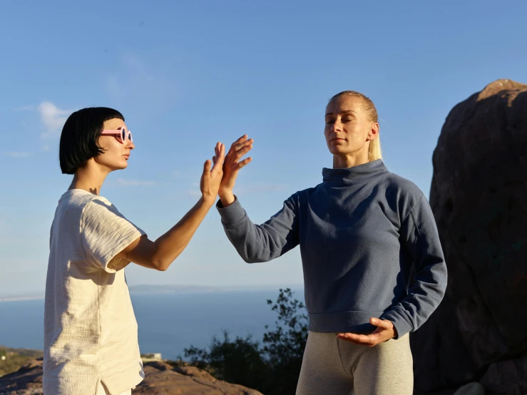 two women in grey pants stand near rocks and look at soing