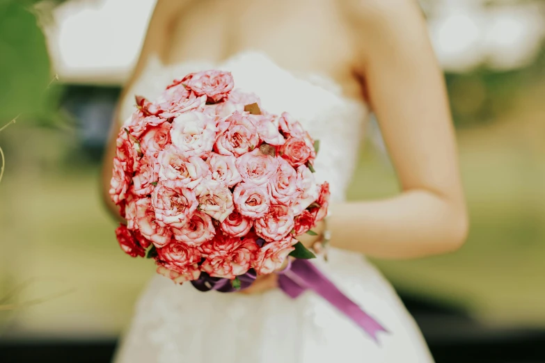 a bride holding a wedding bouquet and standing outside